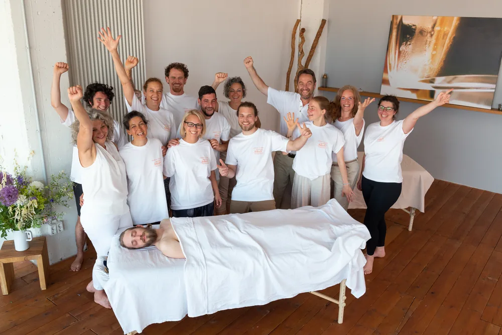 Die ganze Gruppe jubelt mit erhobenen Armen um eine Massageliege
