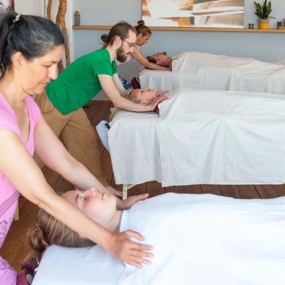 Teilnehmende der Ausbildung arbeiten im Kursraum an mehreren Massageliegen